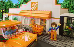 An illustration of a NovaBrix The Home Depot Canada building brick store. A staff member figurine is waving as a customer in a rental truck drives out of the carpark.